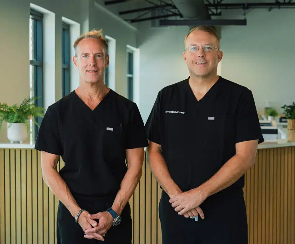 Two male medical professionals in black scrubs standing inside a modern clinic office
